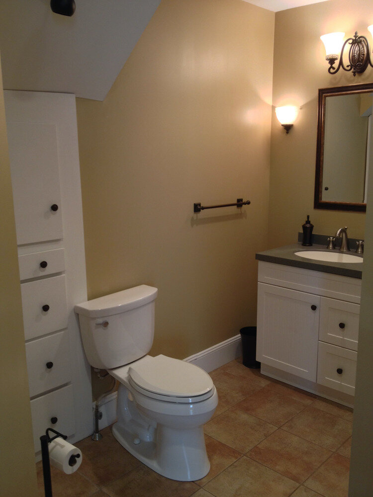 A custom-built tall linen storage cabinet fitted under a sloped ceiling, alongside a white vanity